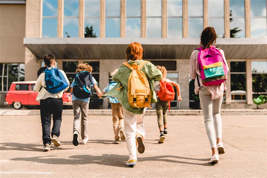 Students with backpacks walking toward a school building